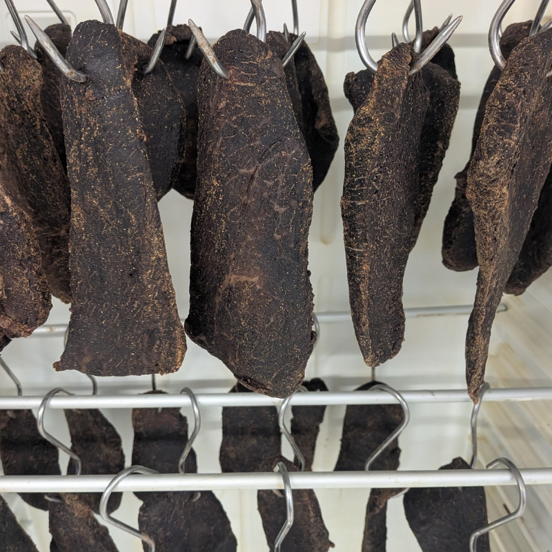 Repen biltong hangen aan haken te drogen in de droogkast van onze slagerij
